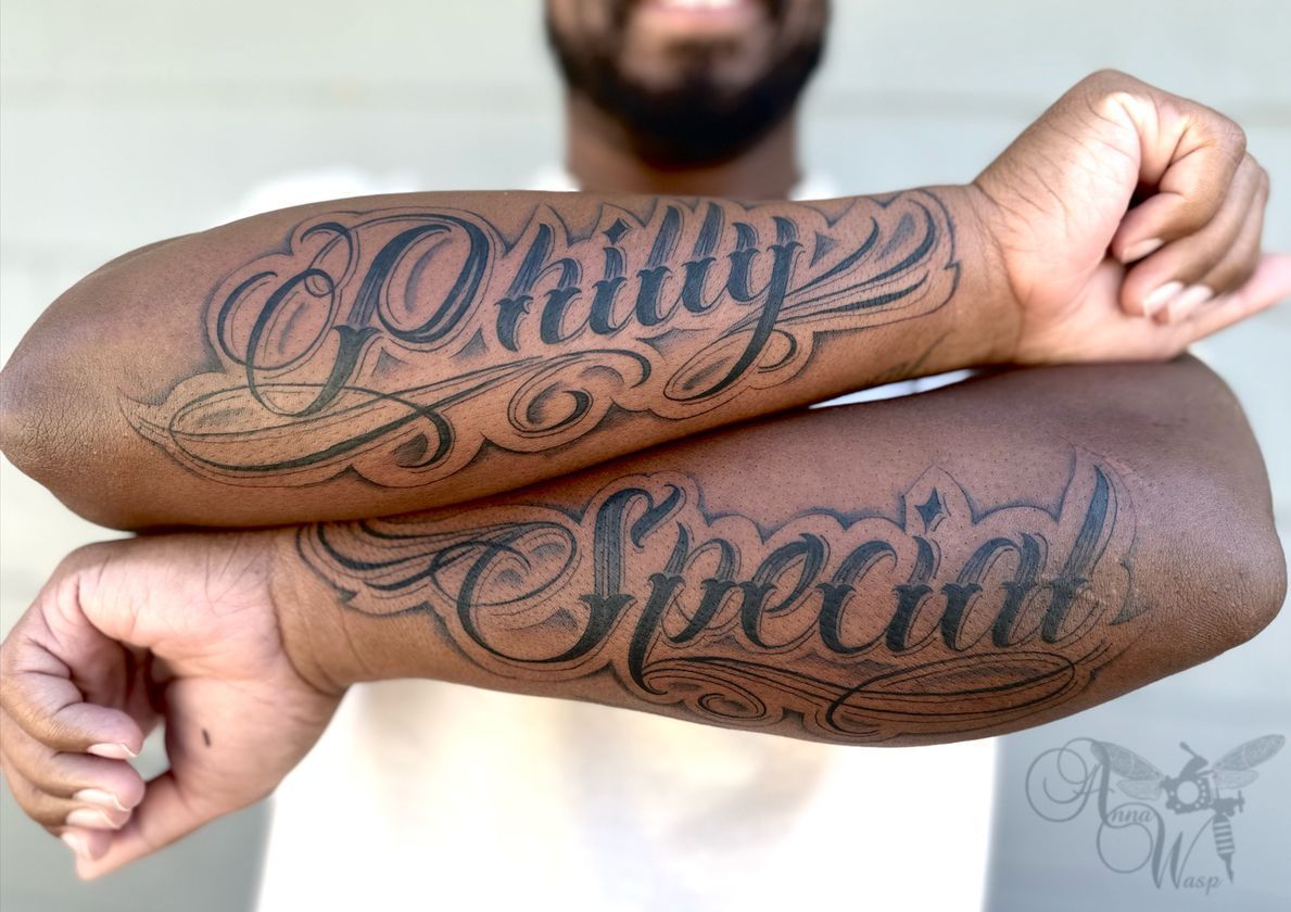 Two black forearms with tattoos. One reads