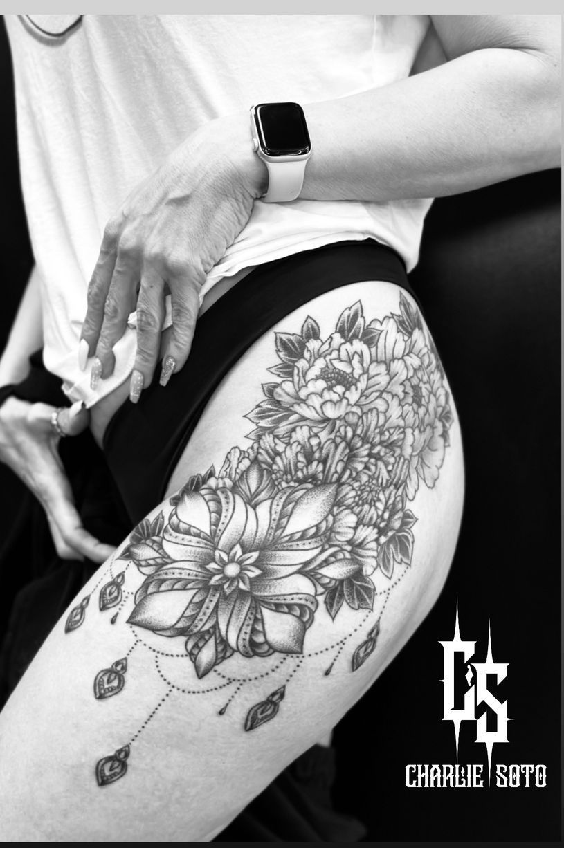 Black and white photo of a person with a floral thigh tattoo, wearing a white top and a smartwatch.