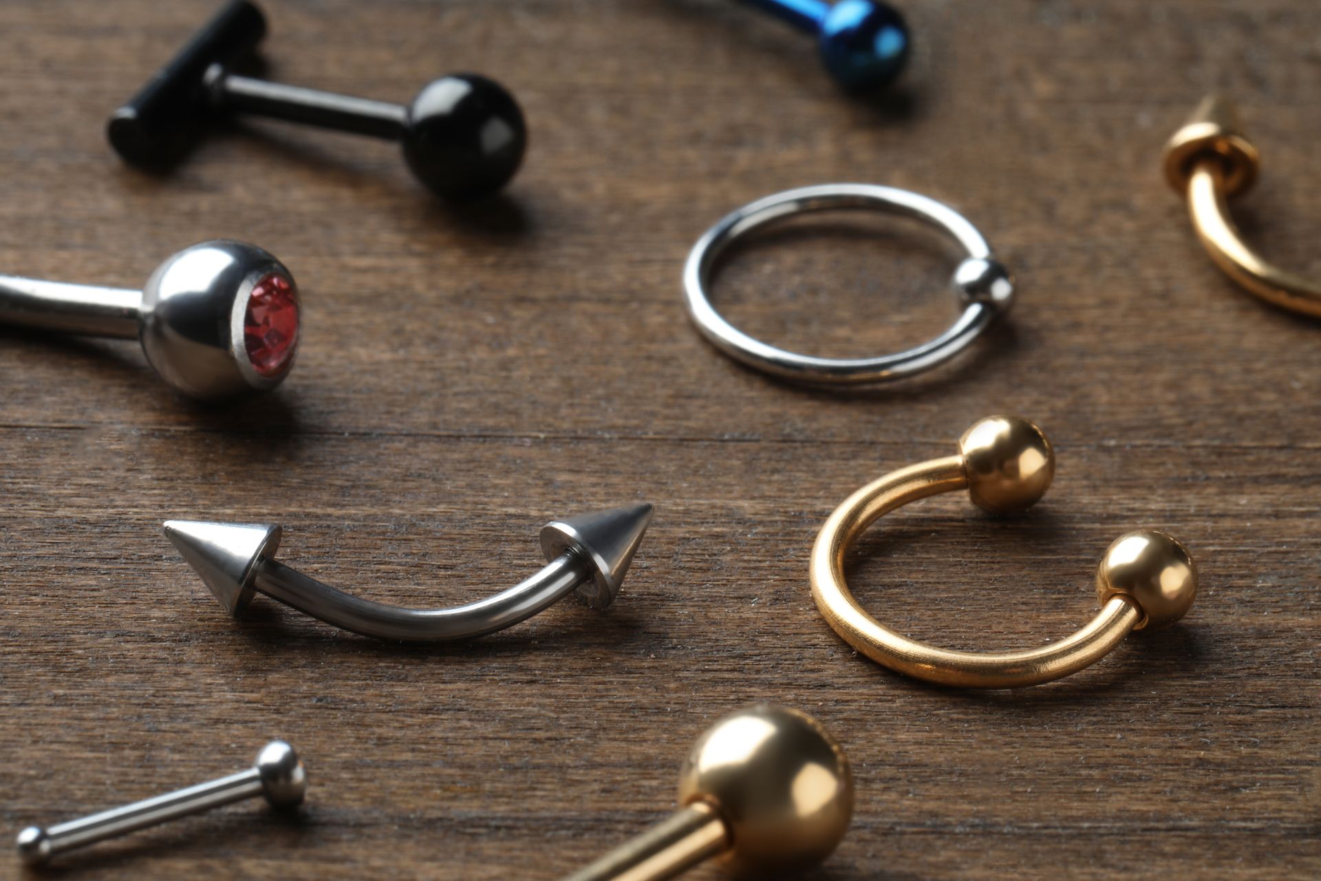 Close-up of various metal body jewelry, including barbells, hoops, and curved pieces on a wooden surface.