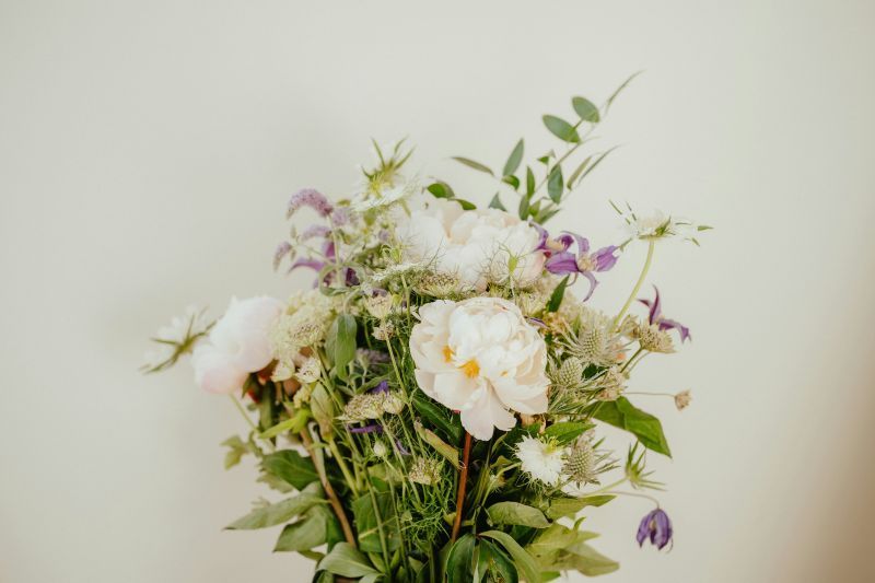 White and purple flowers with green foliage in a bouquet against a plain beige background