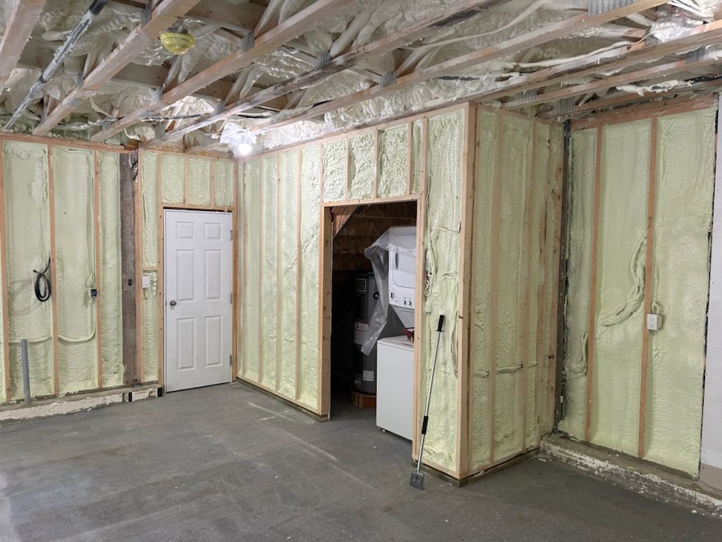Interior room under construction, walls and ceiling insulated with yellow foam, door and unfinished concrete floor visible.