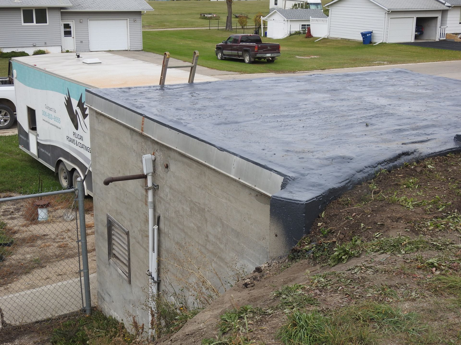 Flat roof building with wet sealant. Rebar sticks up. A trailer and pickup truck are parked nearby.