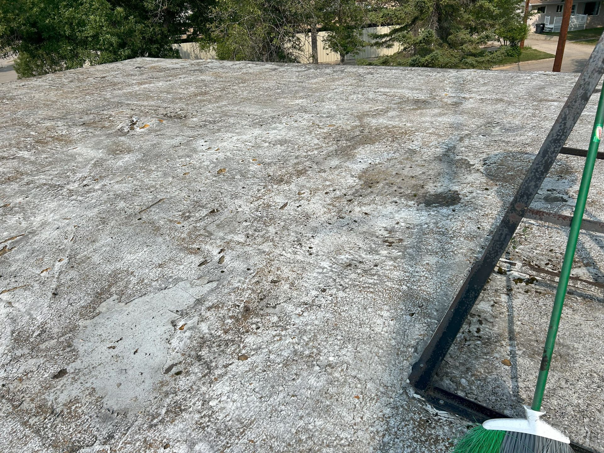 Flat roof with weathered, white granular surface; green broom propped nearby.
