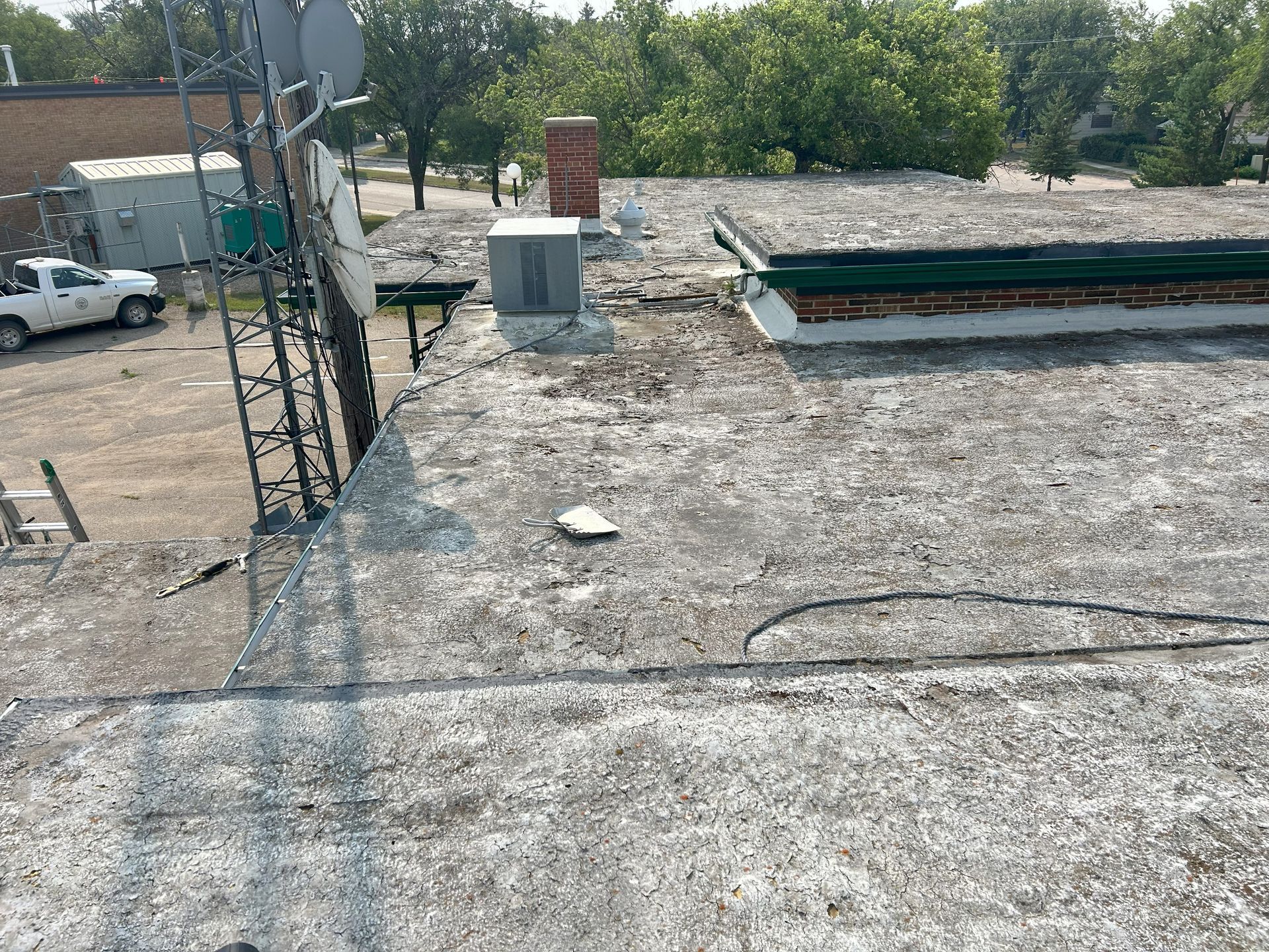 Flat, weathered rooftop with air conditioning unit, chimney, and satellite dishes.