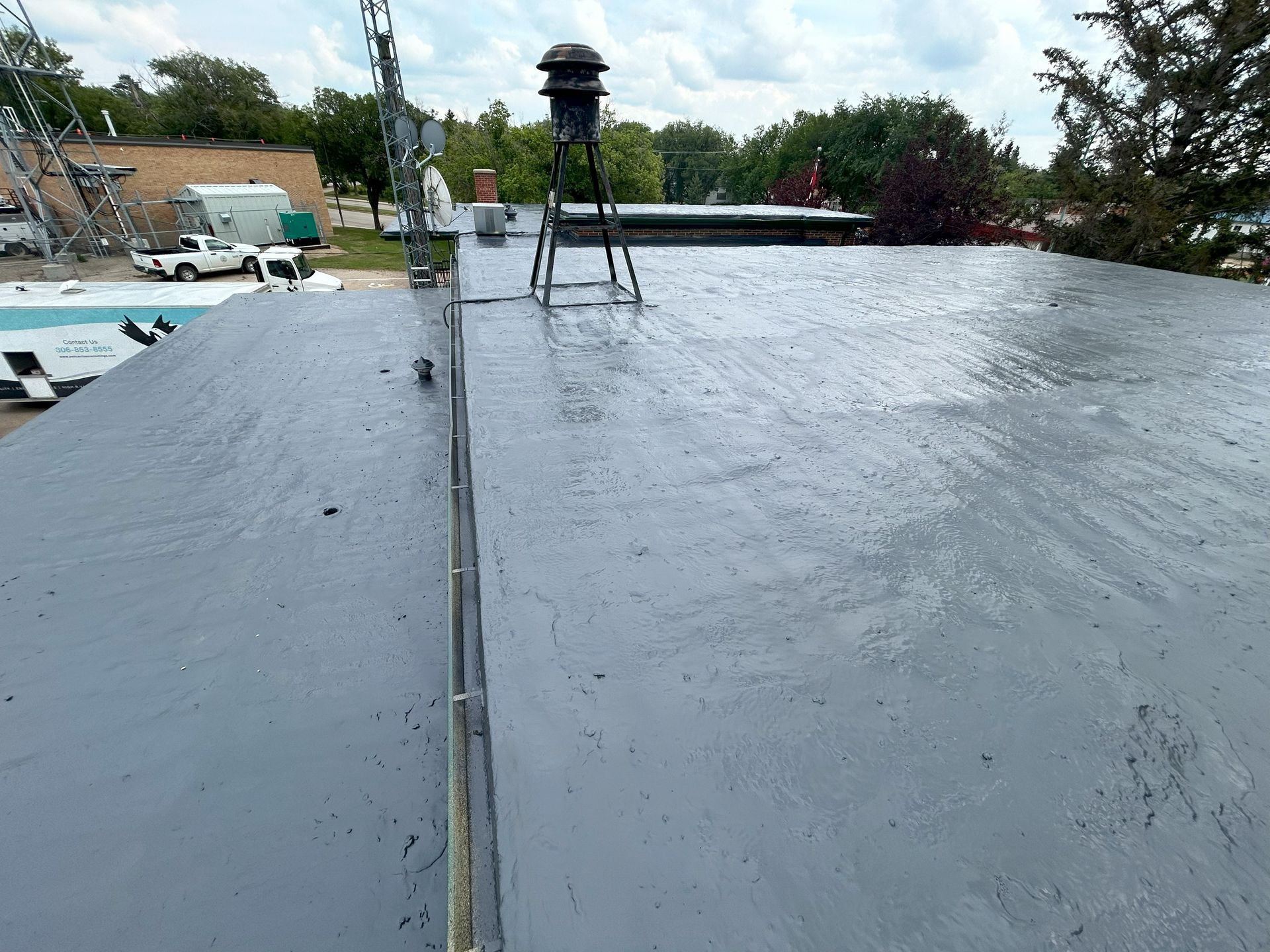 Flat, gray commercial roof with equipment and trees in the background.