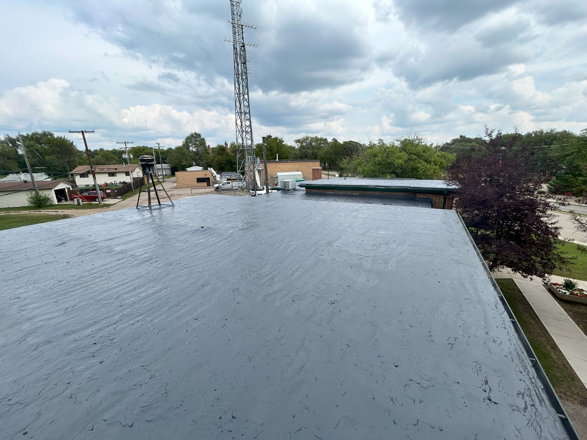 View from a flat, gray roof towards a radio tower and overcast sky.