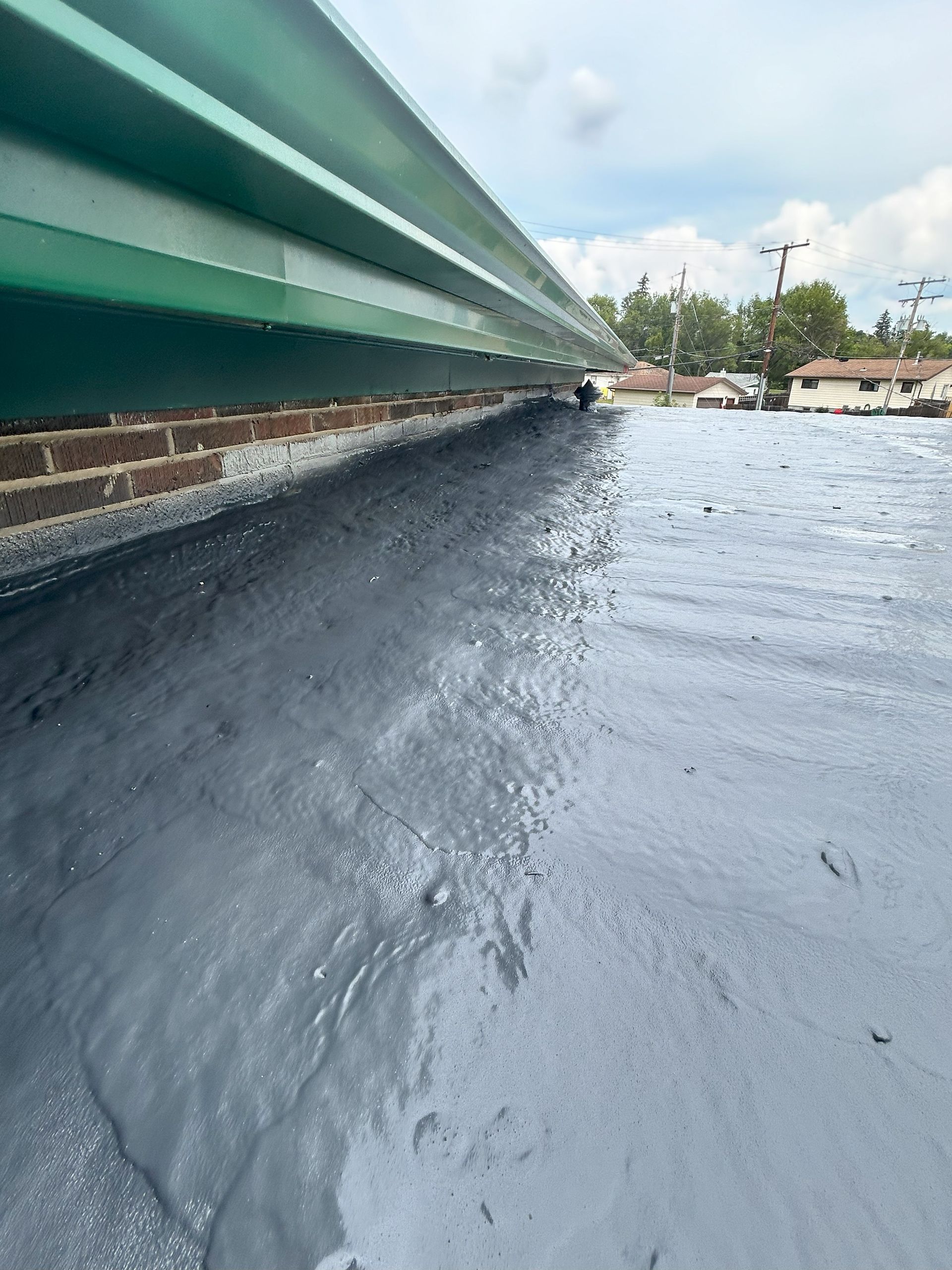 Green corrugated metal overhangs a newly coated, grey roof.