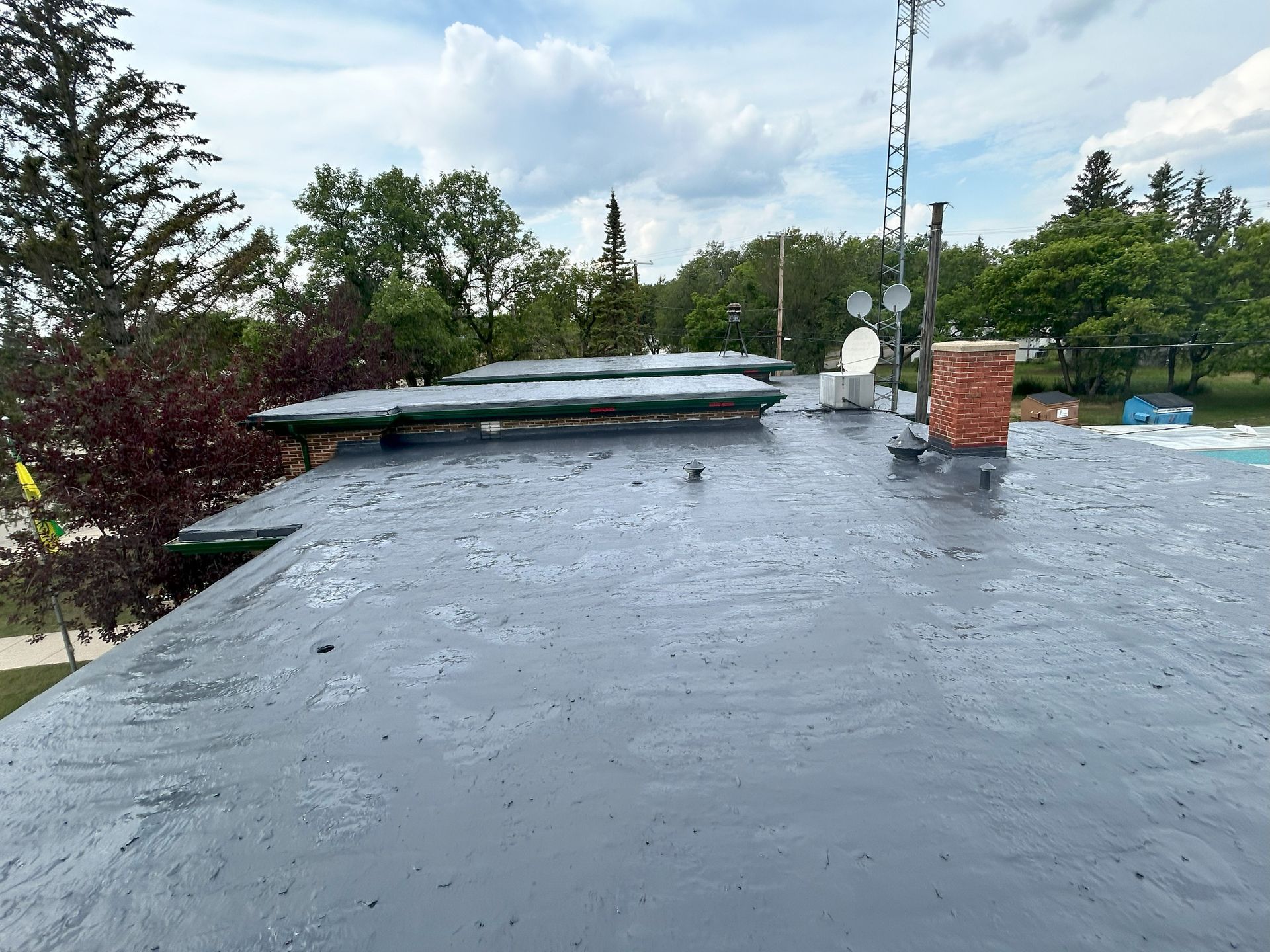 Gray roof with structures and antennas against a cloudy sky, trees in the background.