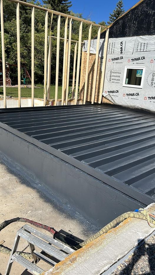 Construction site: grey metal structure with wooden framing, exterior walls in progress under clear sky.