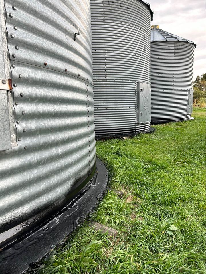 Three silver metal grain silos on green grass.