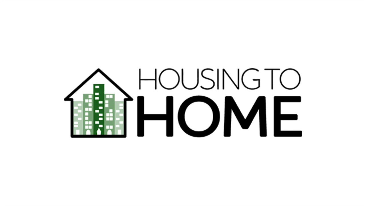 A logo for housing to home with a house and buildings in the background.