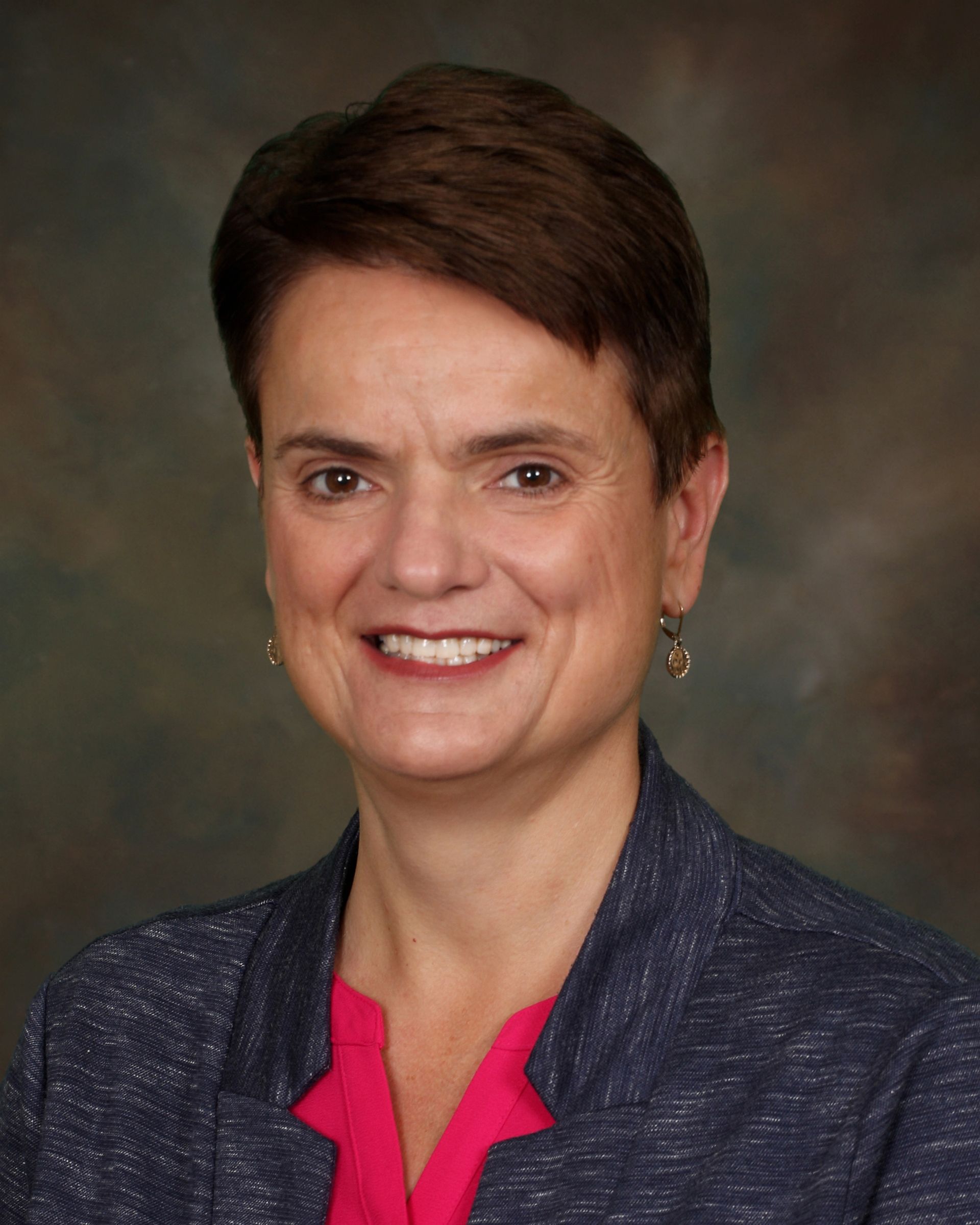 A woman wearing a blue jacket and a pink shirt smiles for the camera.