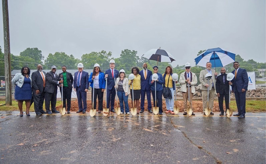 A group of people are standing in the rain holding shovels.