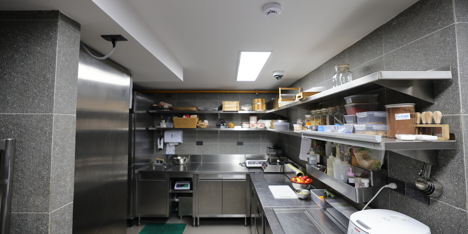 Commercial kitchen with stainless steel counters, shelves, and prep supplies under bright overhead lights