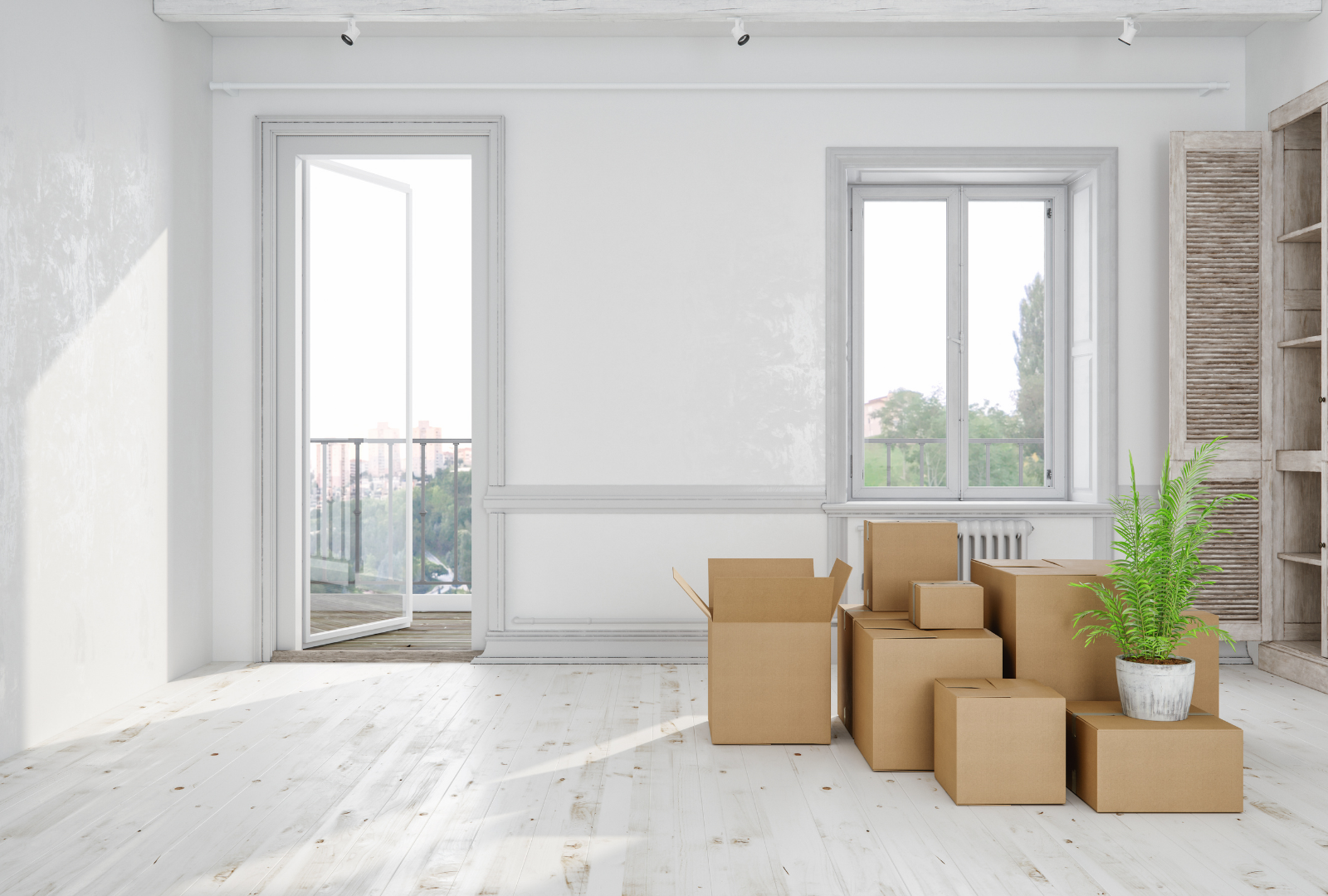 Bright empty room with white walls, large windows, and stacked cardboard moving boxes near a potted plant
