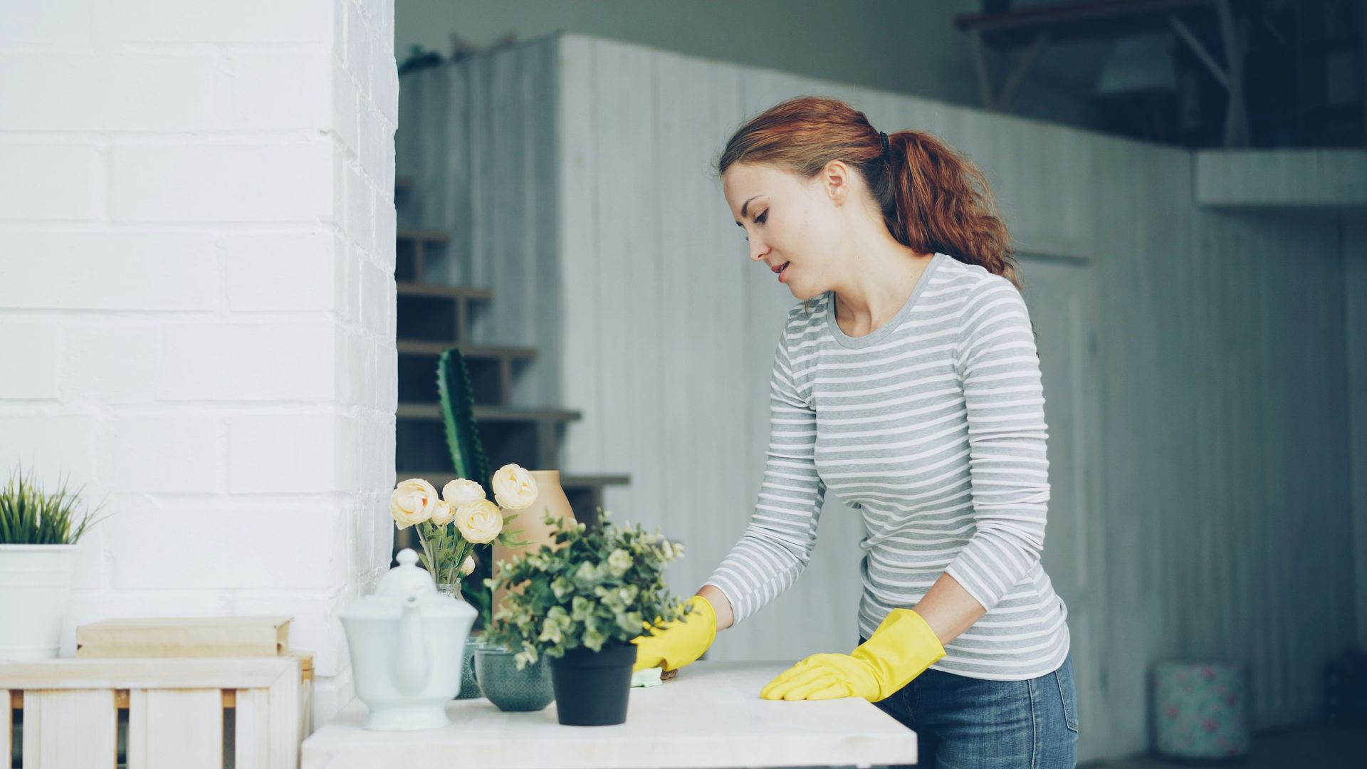 Person in yellow gloves arranging flowers on a table in a bright kitchen or workshop