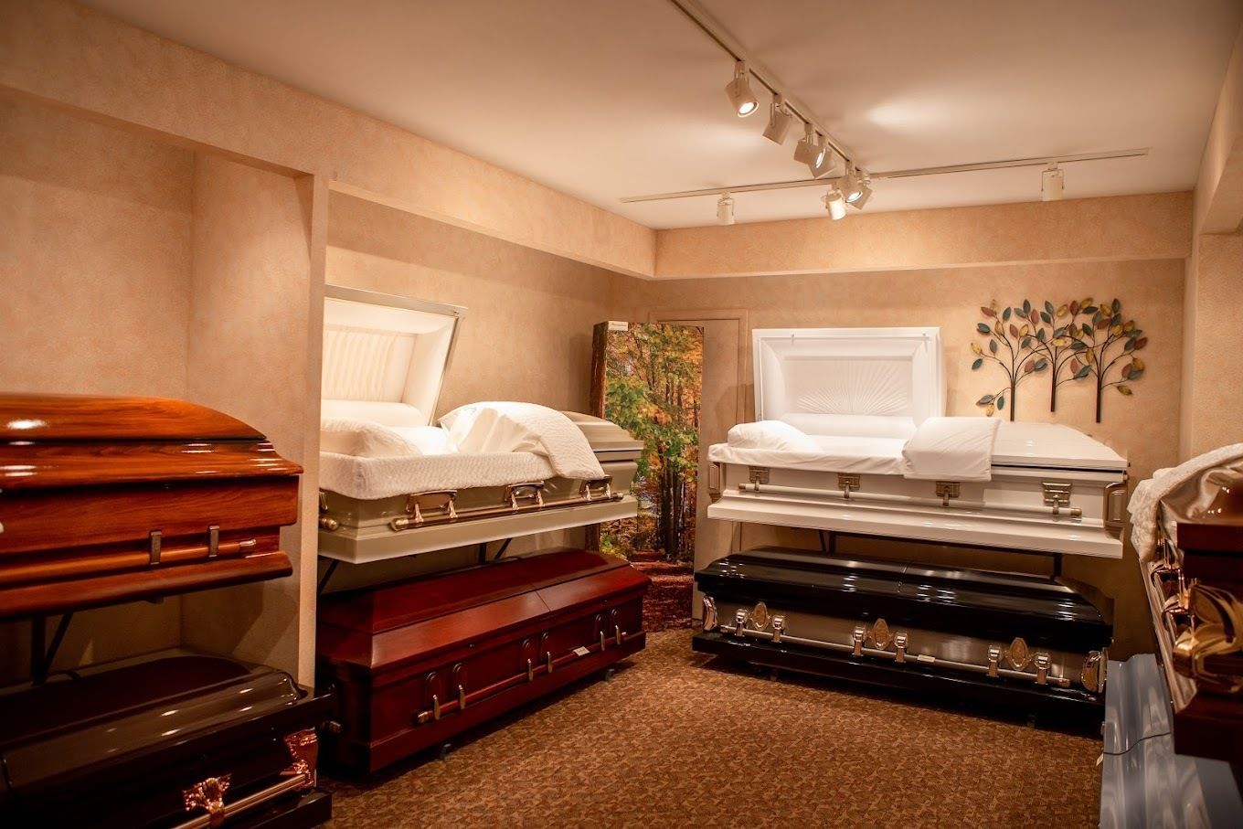 A showroom display featuring several open and closed wooden and metal caskets arranged in a carpeted room with spotlights.