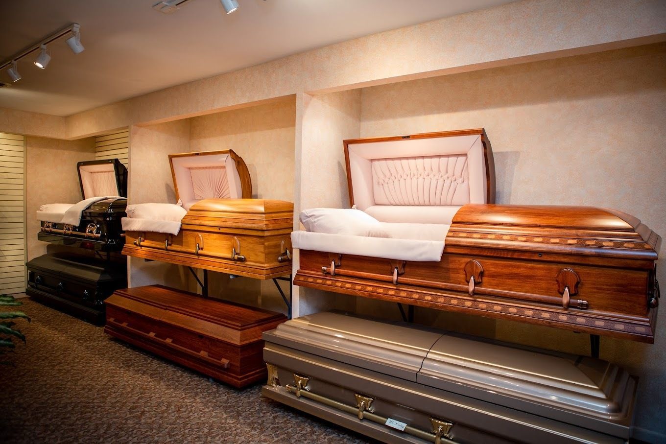 A showroom displaying several open and closed wooden and metal caskets on stands in a room with recessed lighting.