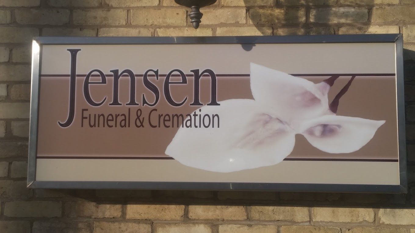 A sign for Jensen Funeral & Cremation with a white lily graphic on a brick wall background.