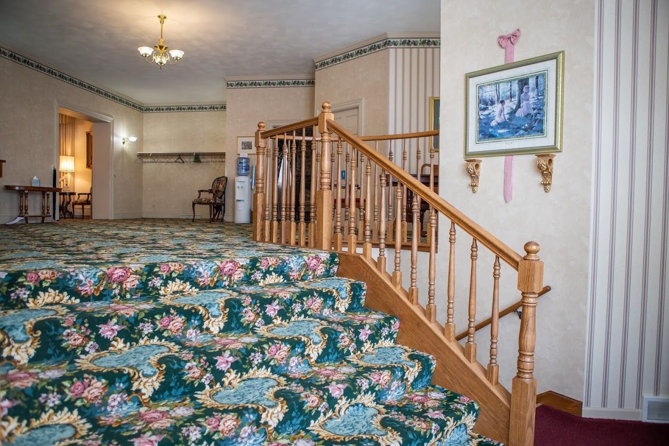 Carpeted stairs with a floral pattern lead up next to a wooden railing in a room with patterned wallpaper.