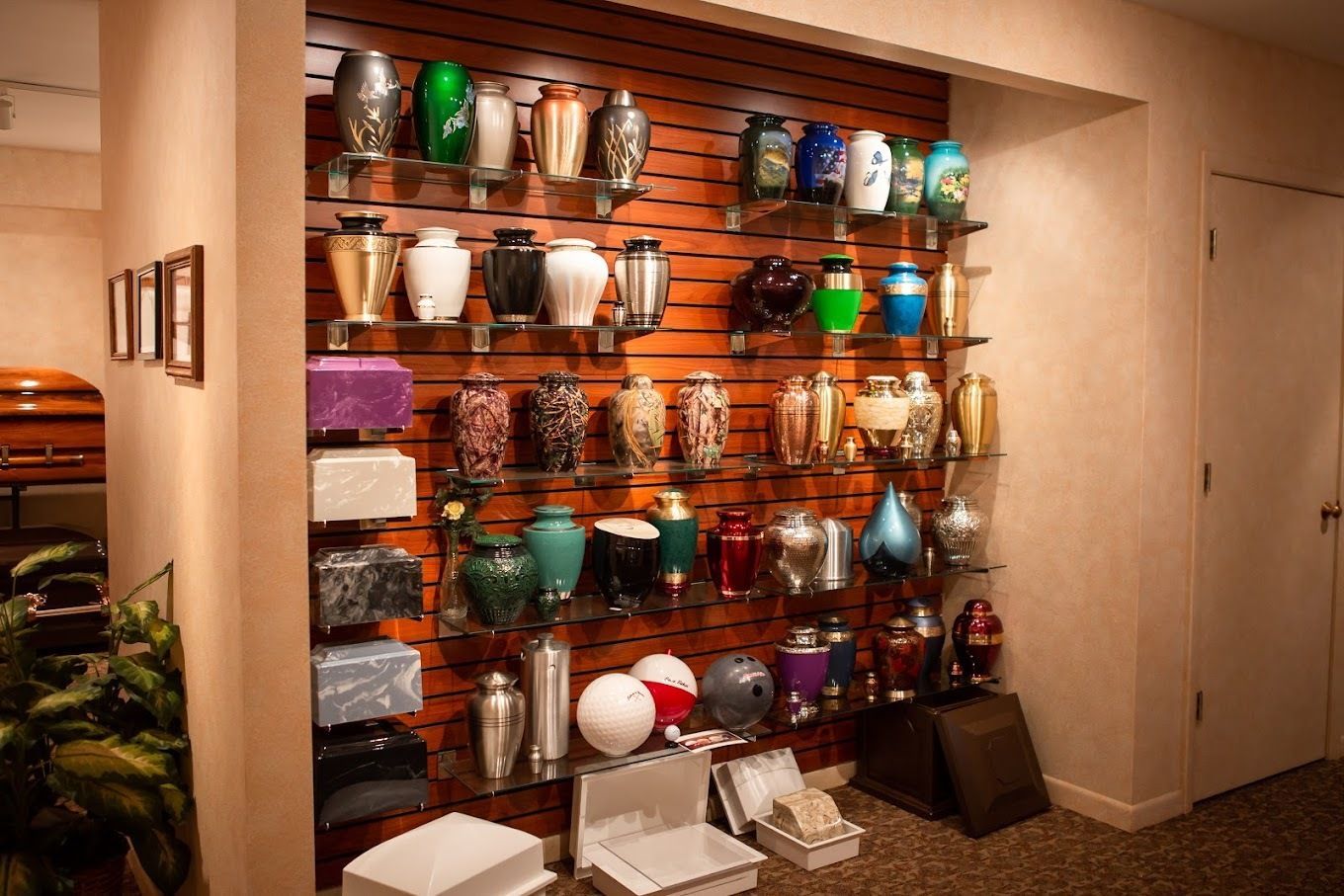 A display wall in a funeral home featuring rows of various decorative cremation urns on glass shelves.