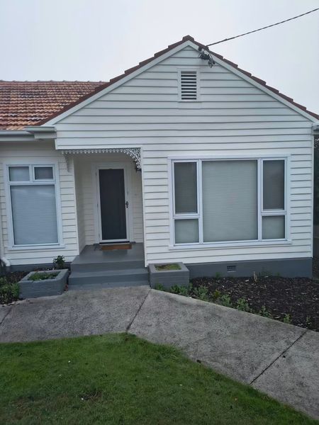 Small white house with a tiled roof, front porch, and curved concrete walkway leading to the door.