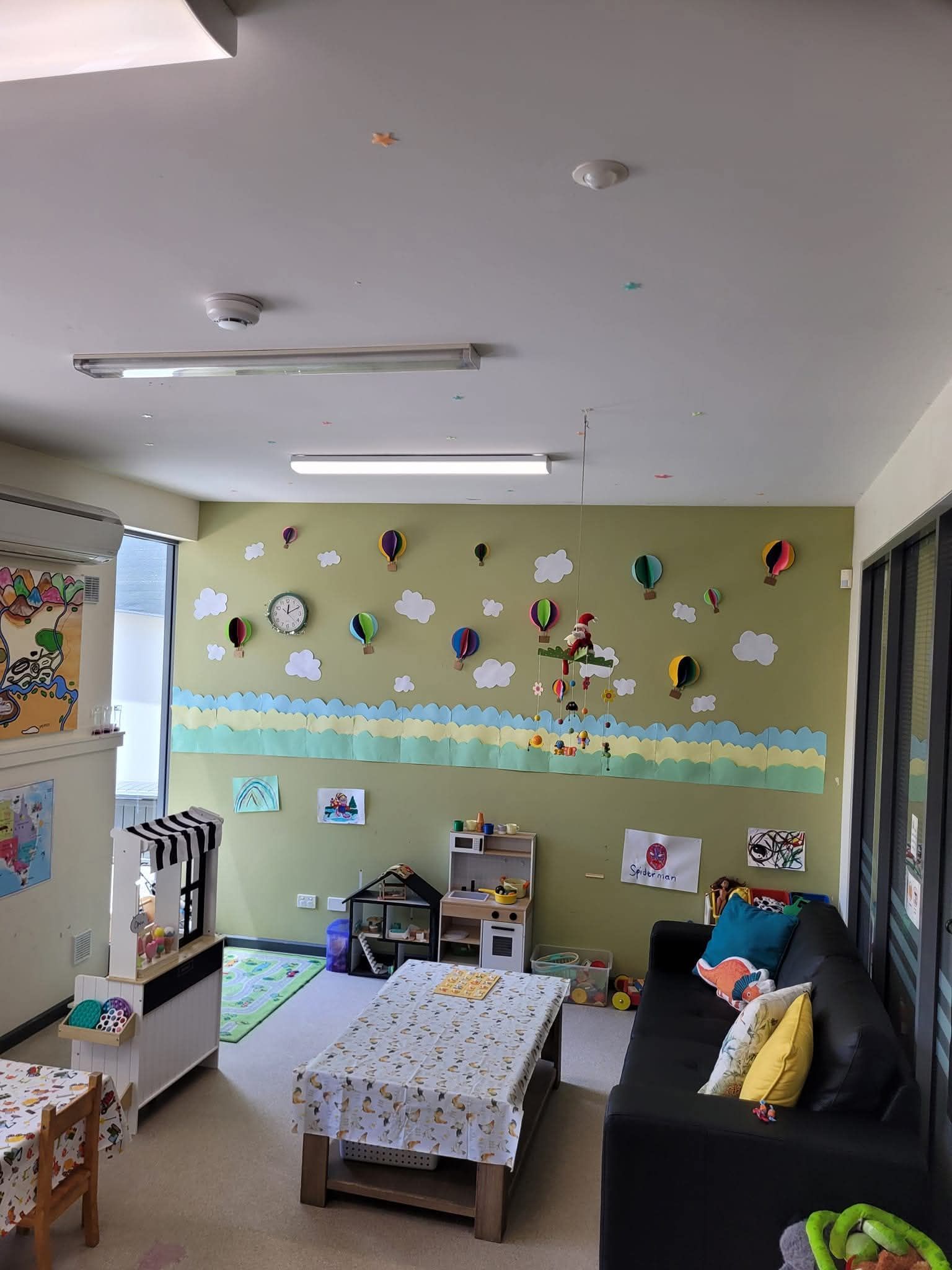 A colorful daycare playroom with a sofa, small table, toys, wall art, and children’s decorations.