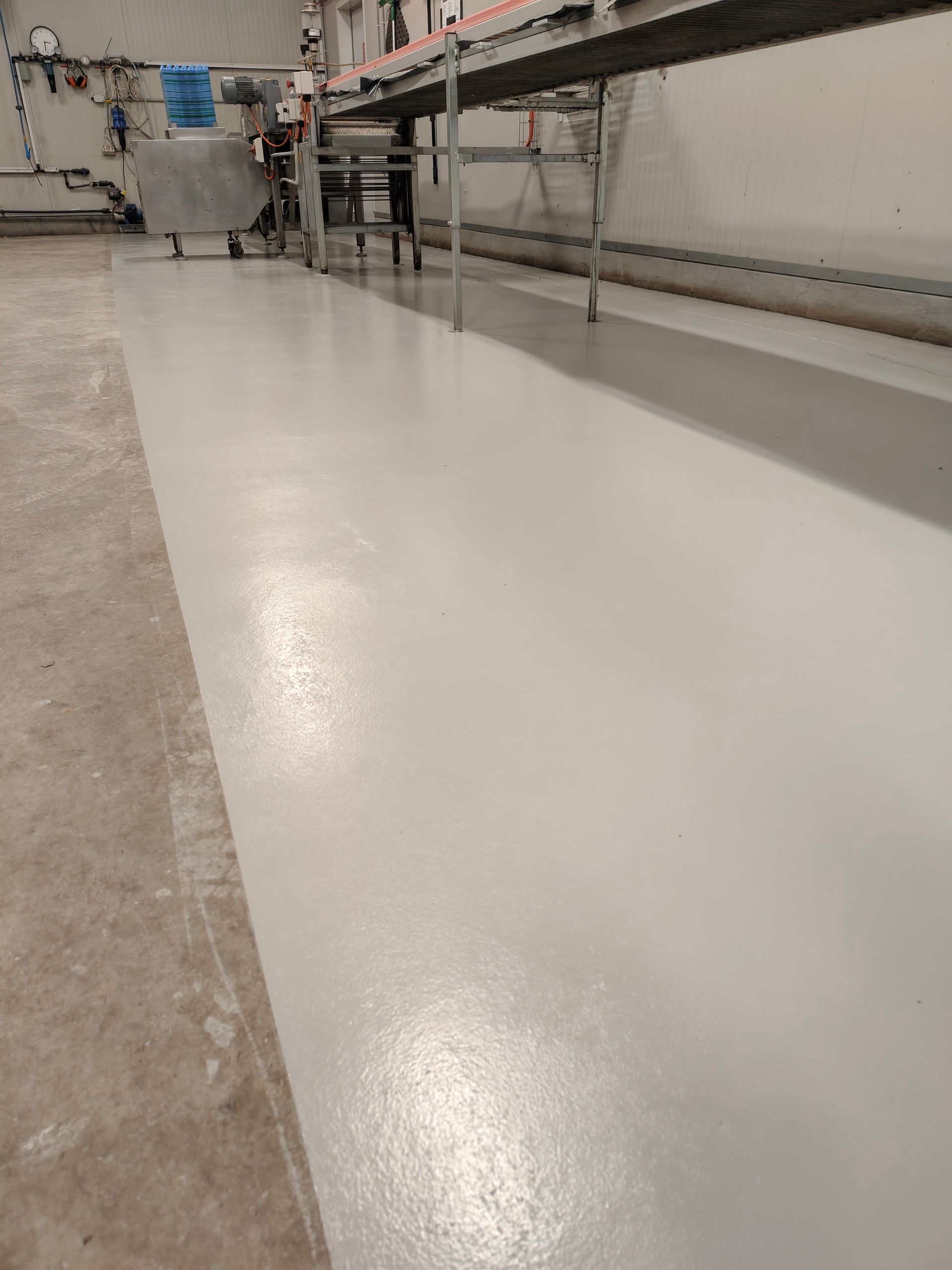 Large white industrial floor in a factory or warehouse, with machinery along the walls.