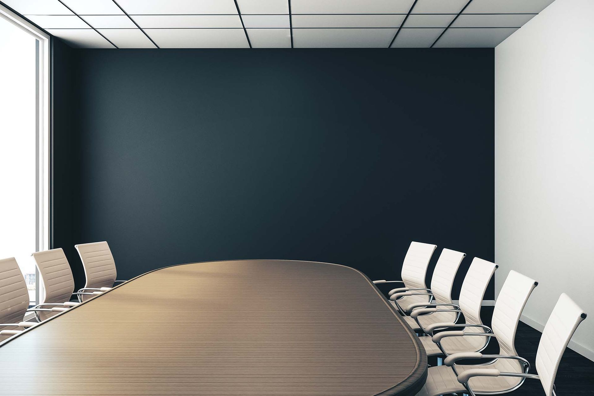 Empty conference room with a long wooden table and white chairs against a dark blue wall.