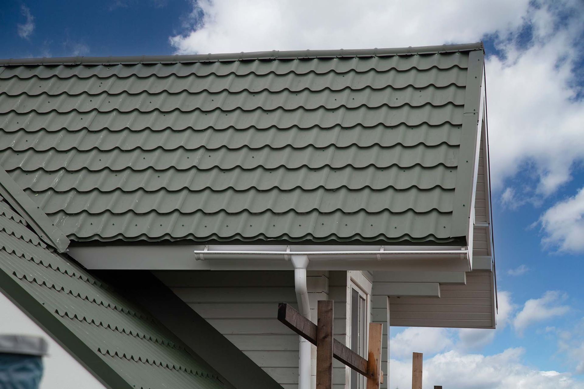 Close-up of a house roof with green shingles and white gutters against a blue sky