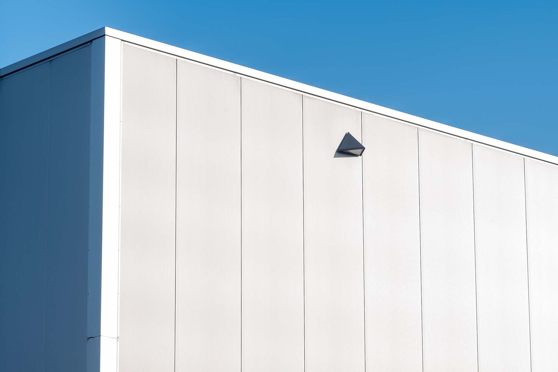 White building facade under a clear blue sky, with a small wall-mounted light