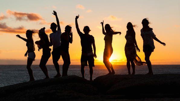 A group of people are standing on a beach at sunset.