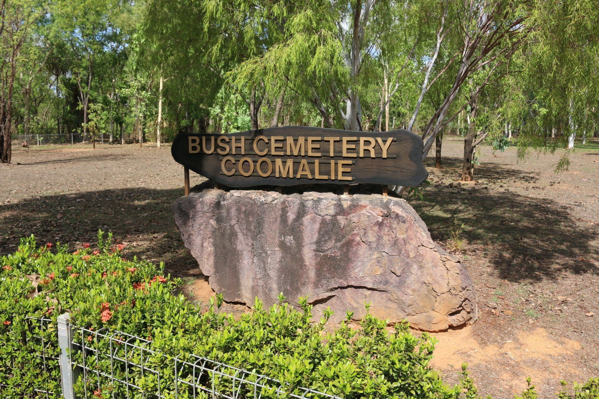 A sign for bush cemetery coomalie is sitting on top of a large rock.