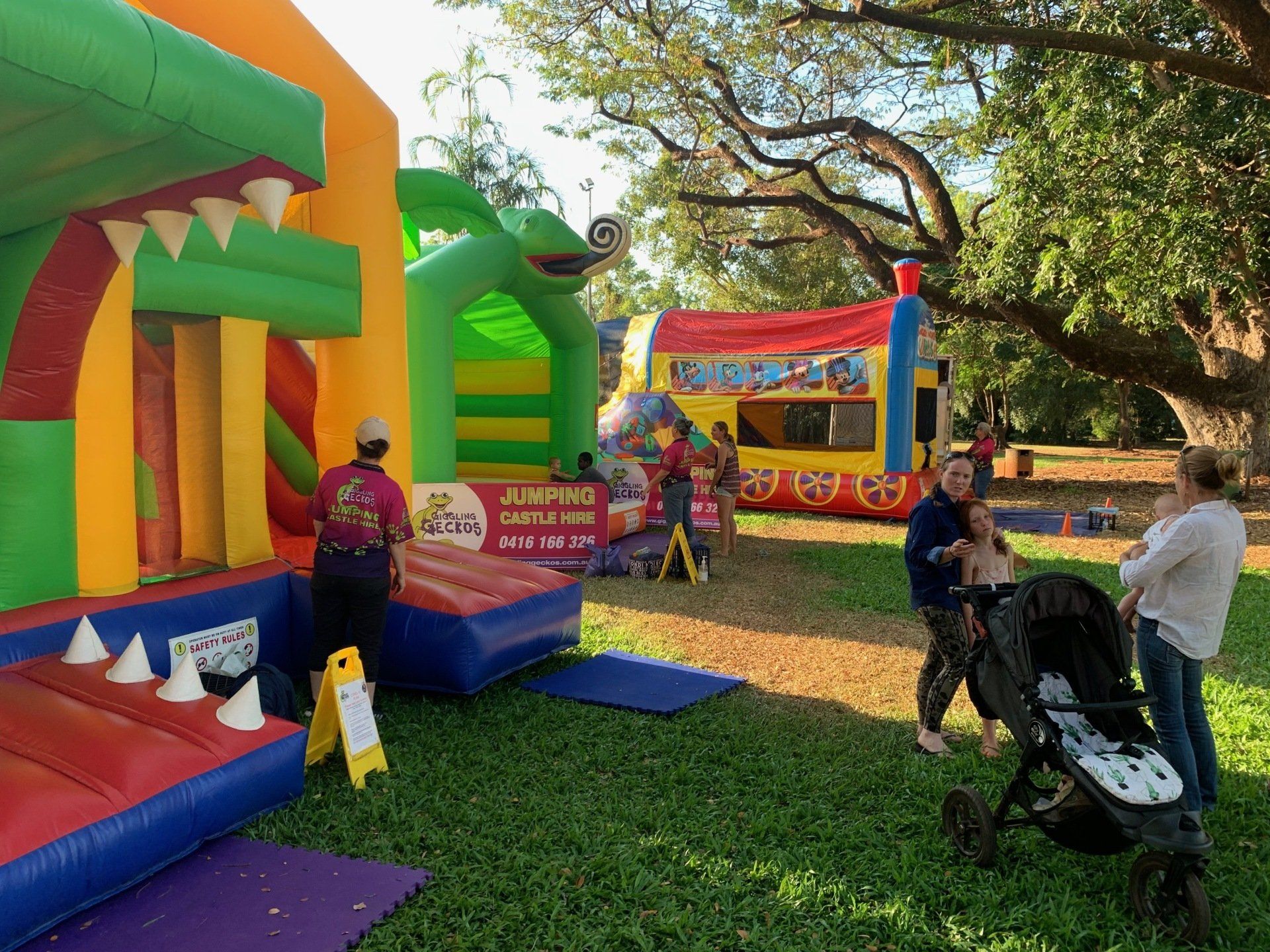 A group of people are standing around a bouncy house in a park.