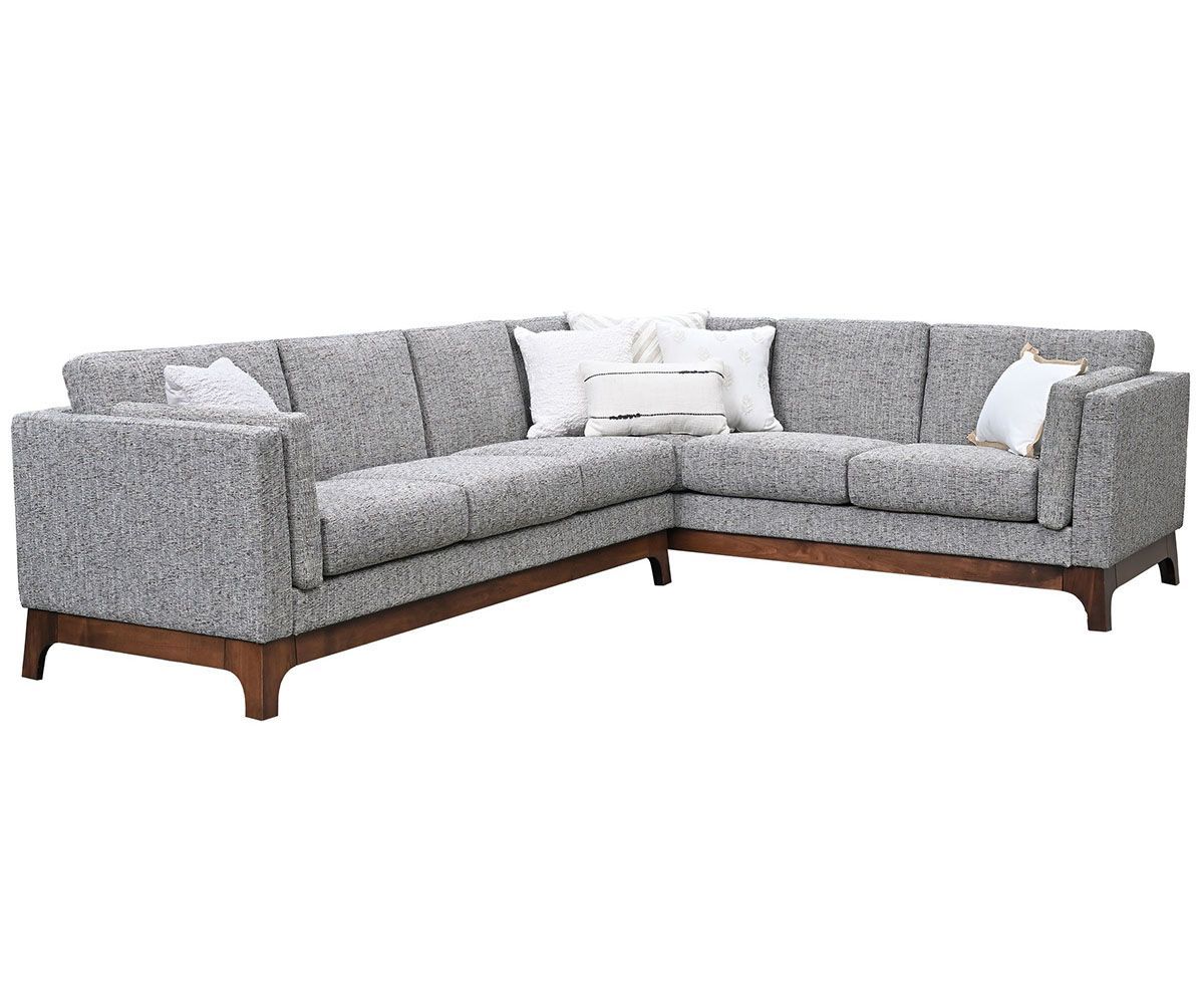 L-shaped gray fabric sofa with wooden legs and several white pillows.