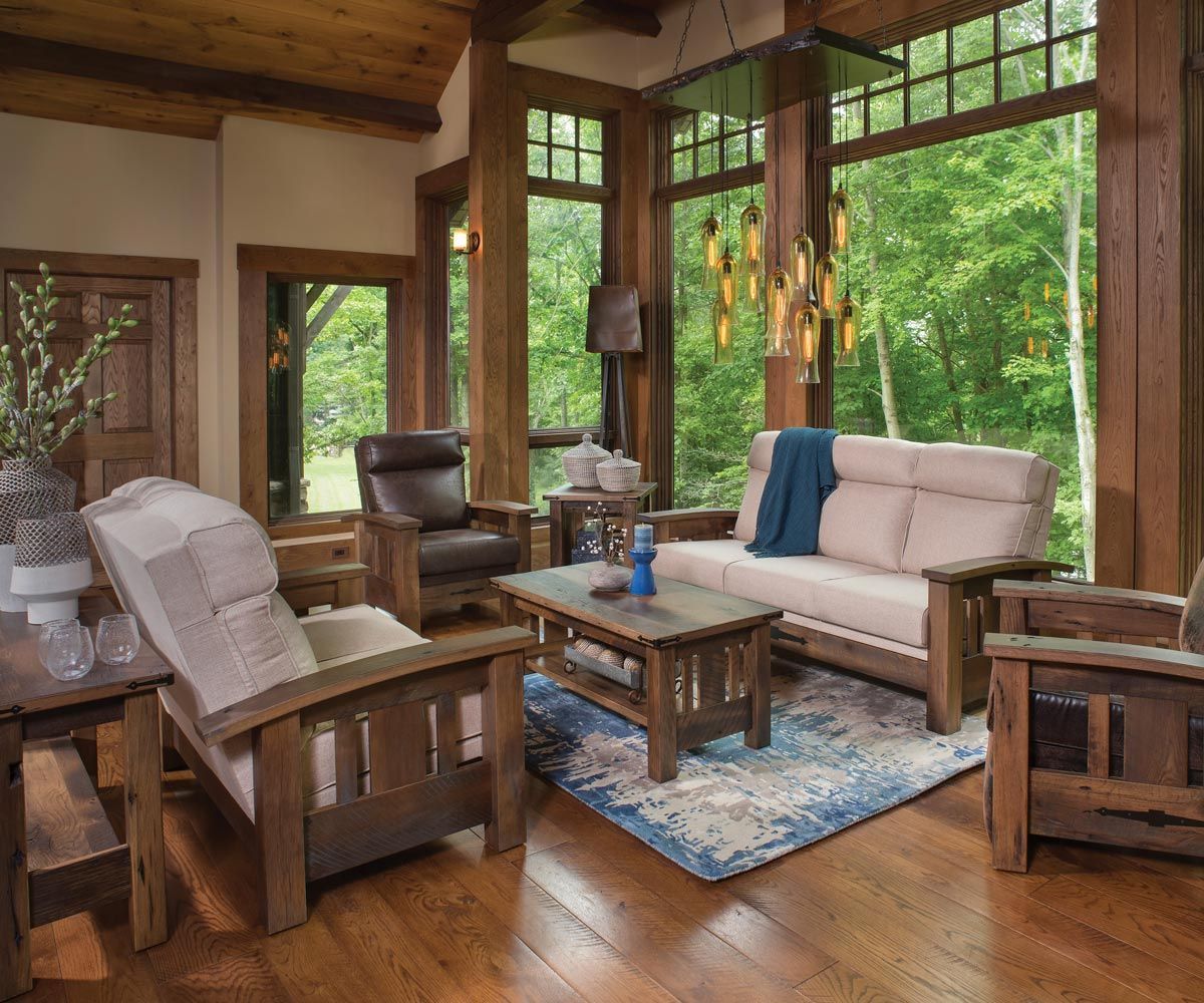 Rustic living room with wooden furniture and large windows overlooking a forest.
