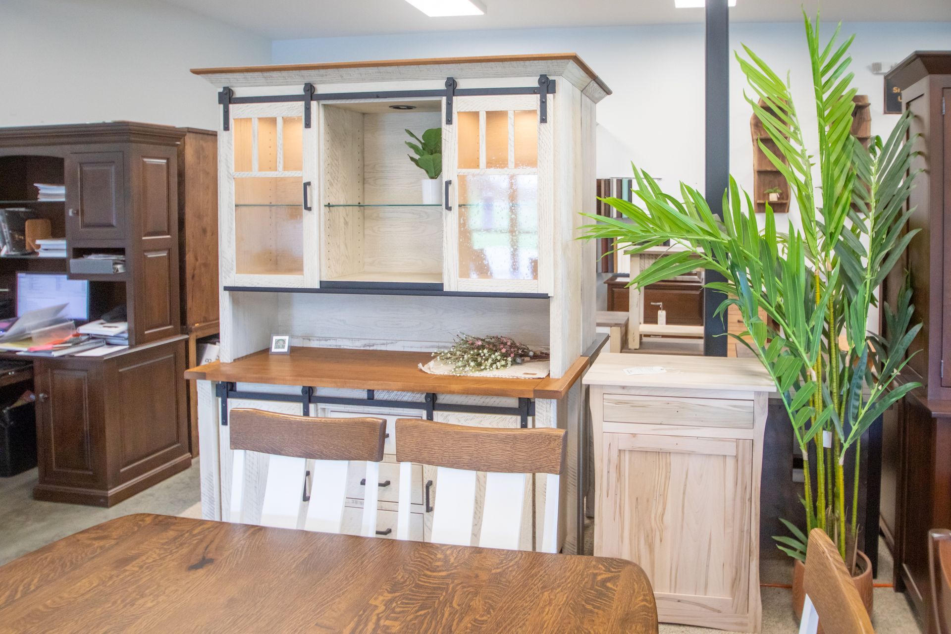 A display of white rustic furniture including a hutch, small cabinet, and table with chairs in a store.
