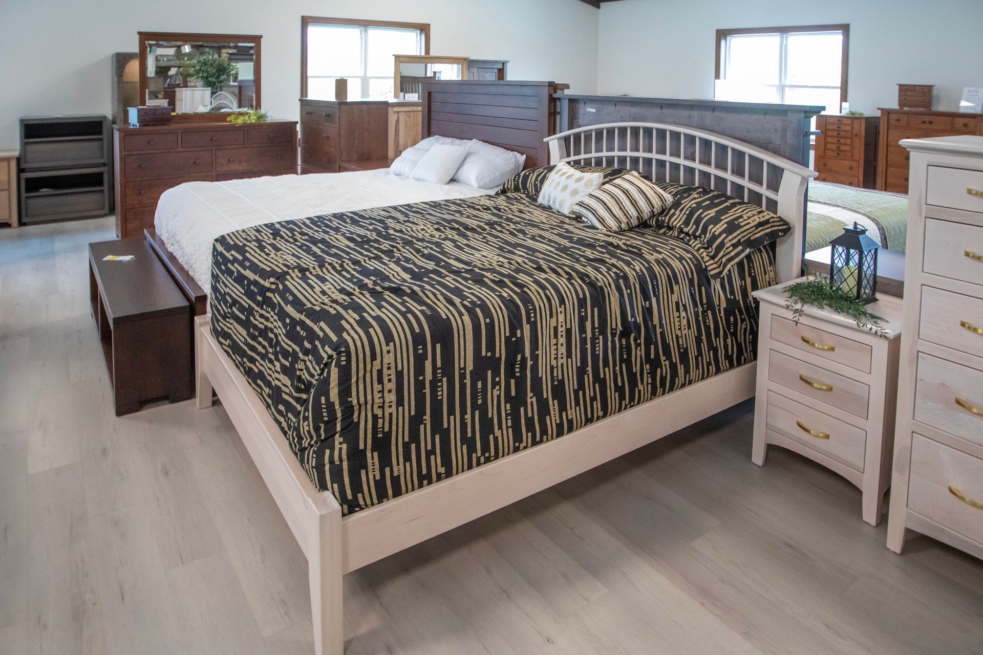 Bedroom furniture showroom, beds with different styles and bedding. Wooden dresser and nightstand visible.