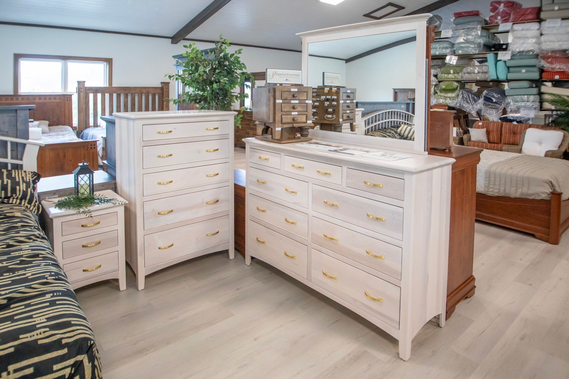 Bedroom furniture display in a showroom, featuring a light-colored dresser, nightstand, and bed.