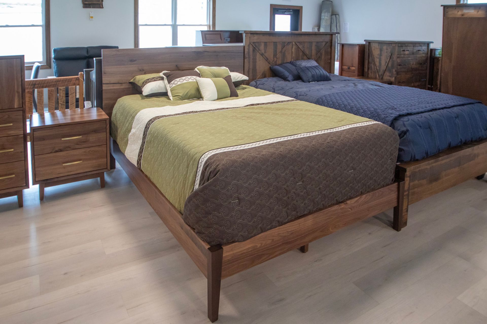 Wooden beds with bedding in a showroom. One bed has green and brown quilt, another has blue.