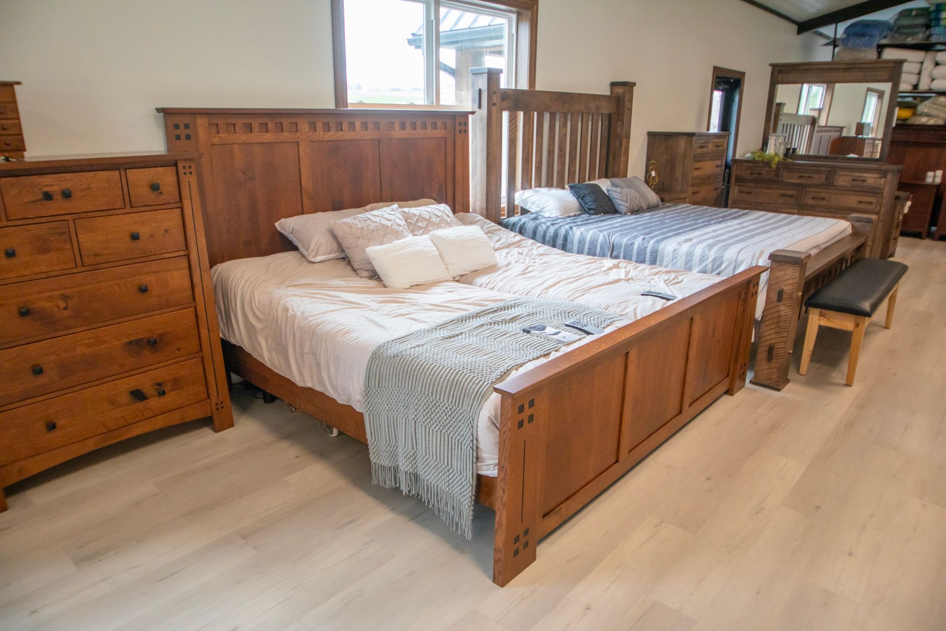 Bedroom furniture display: beds, dressers, and a bench in a showroom with wood flooring.