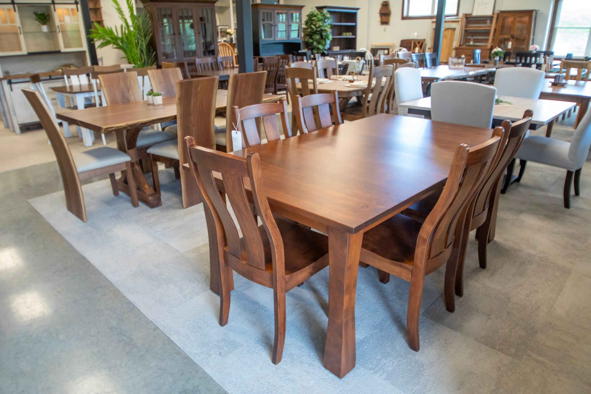 A furniture showroom displaying several wooden dining tables and chairs on a light-colored rug.