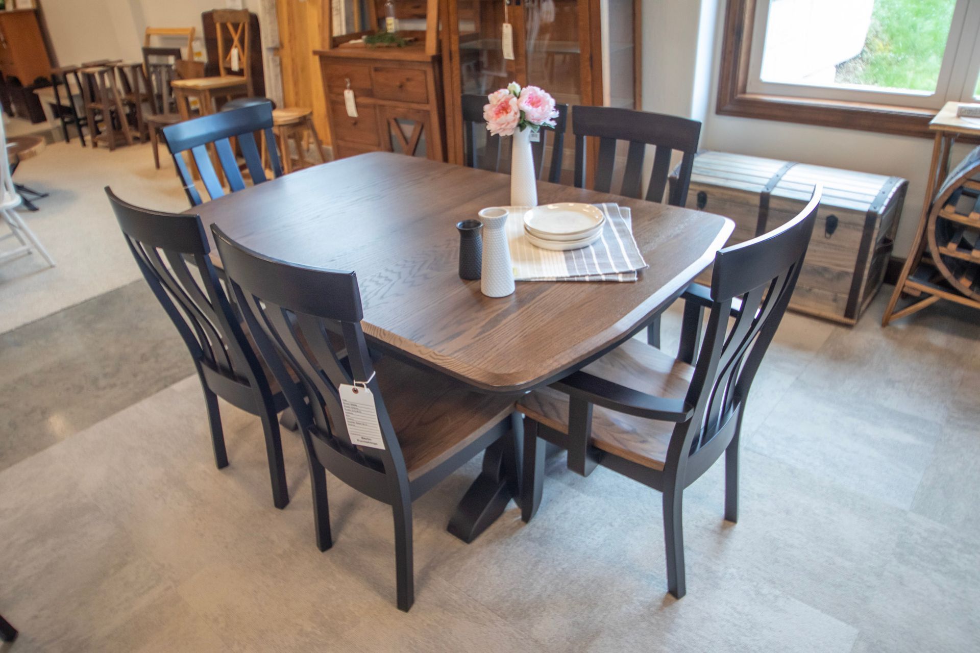 Dining table with six chairs, flowers, and place settings, in a showroom setting.