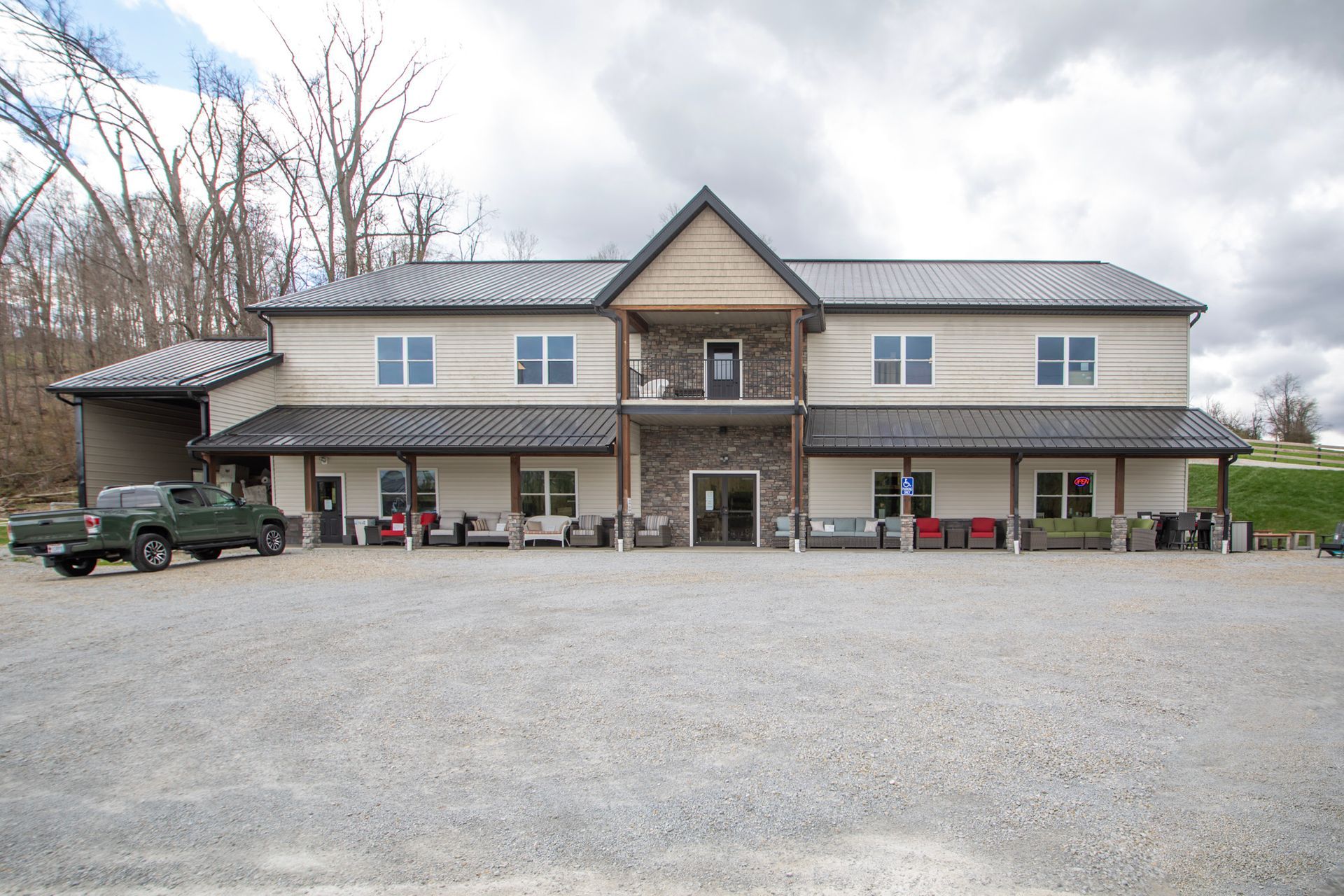 Two-story building with gravel parking lot. Tan and stone facade with a dark metal roof. Trees in the background.