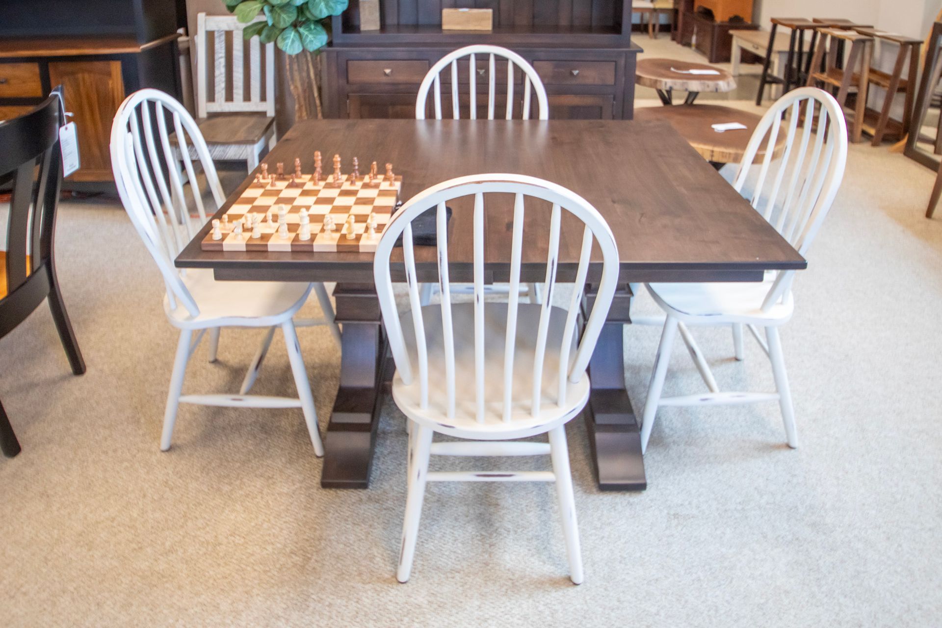 Dining table with four white spindle-back chairs. A chess set sits on the table. The table is brown.