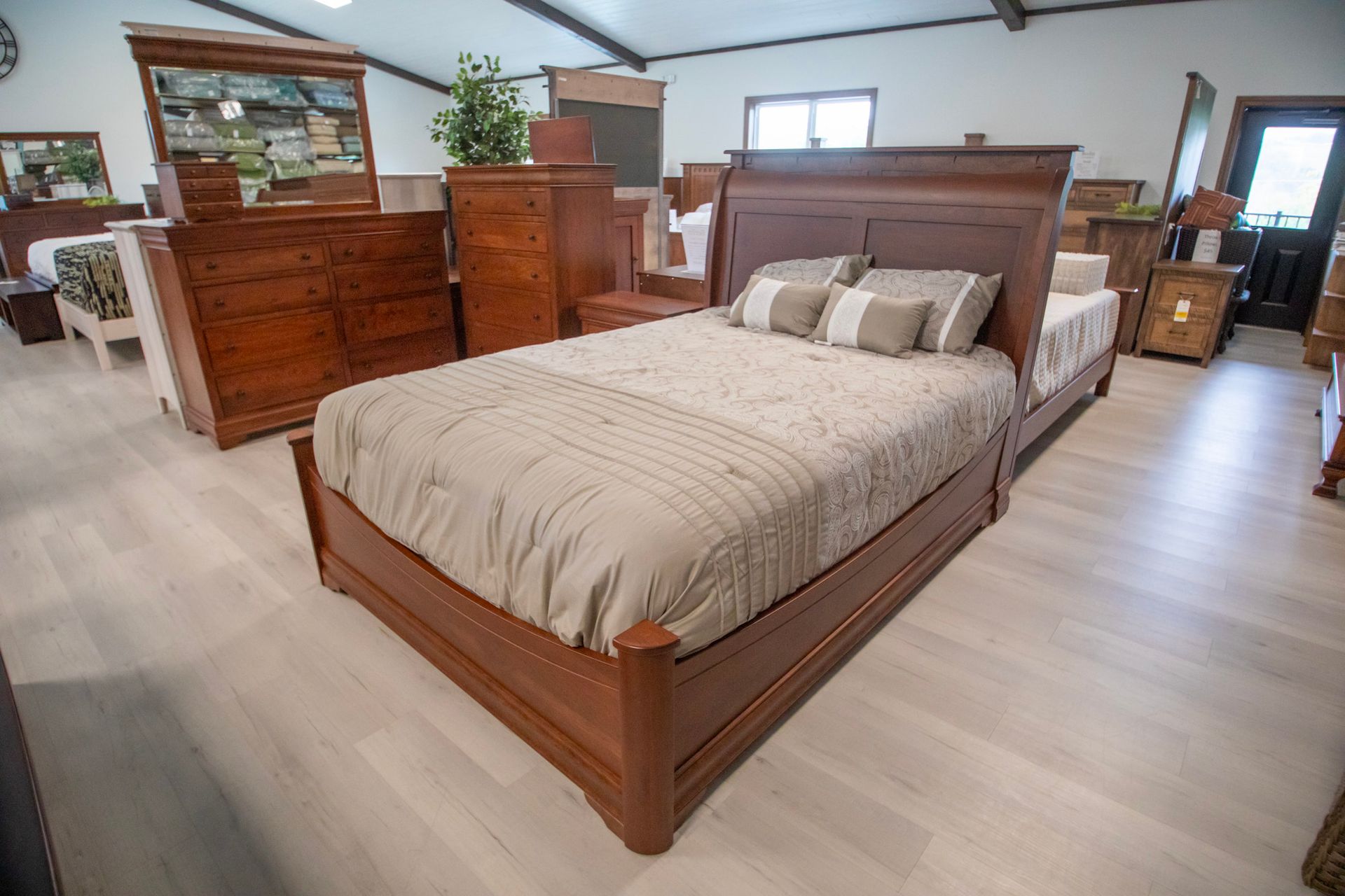 Bedroom furniture showroom with a bed, dresser, and nightstand in natural wood tones.