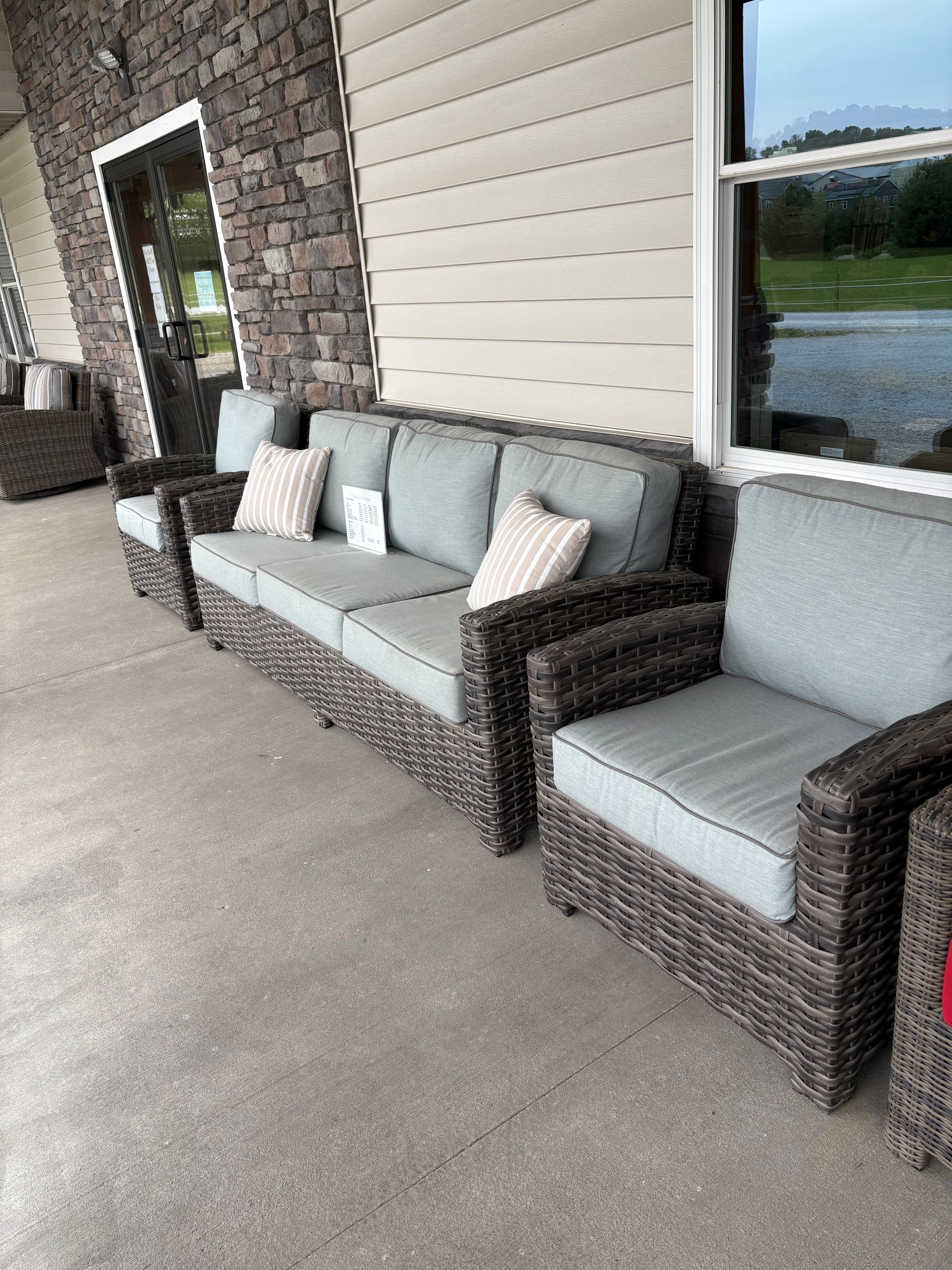 Outdoor wicker furniture set on a porch: blue cushions, gray wicker, stone wall backdrop.