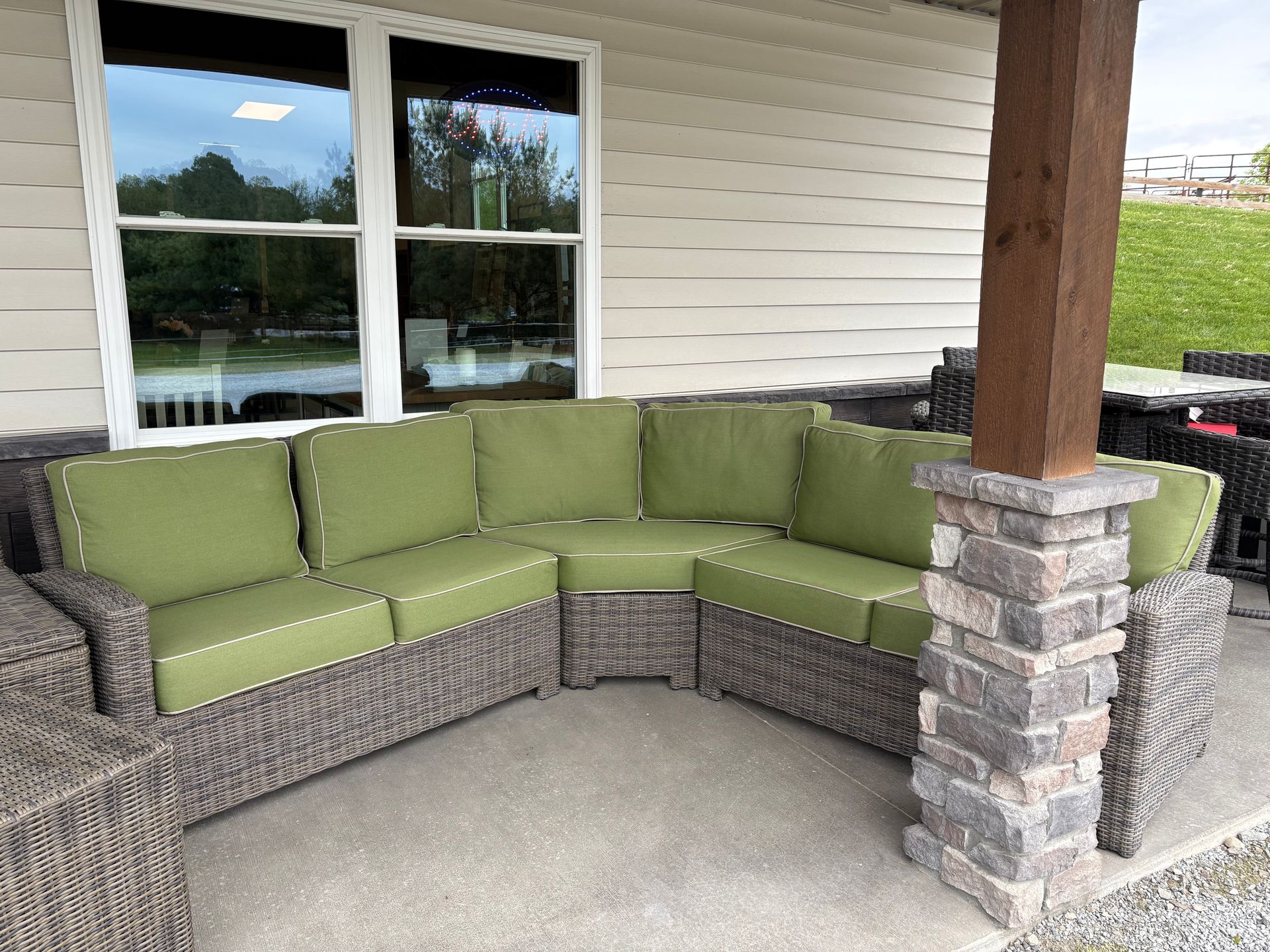 Curved wicker outdoor sectional sofa with green cushions on a patio.