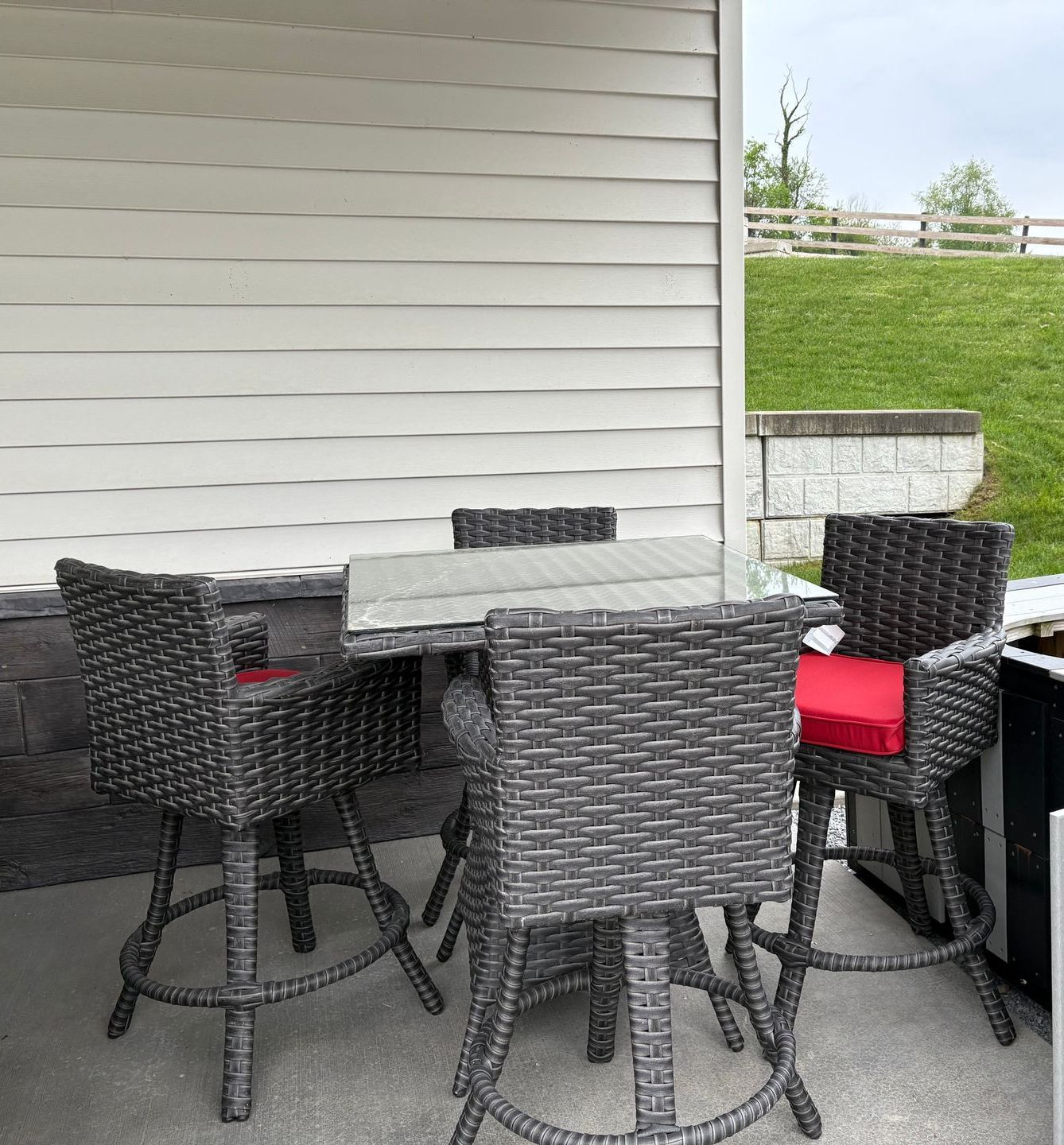 Patio set with gray wicker chairs and a glass-top table on a concrete patio.