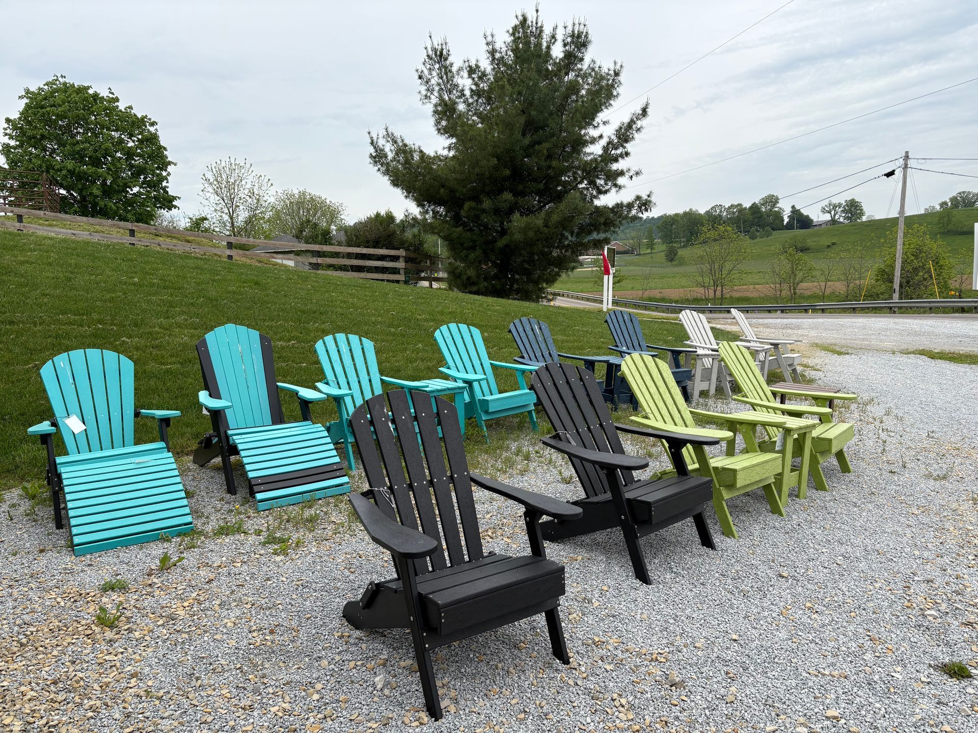 Row of colorful Adirondack chairs on gravel, outdoors. Teal, black, and lime green chairs visible.